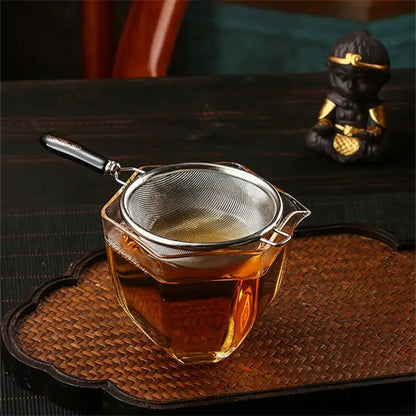 Hand holding stainless steel tea strainer over a cup of brewed tea