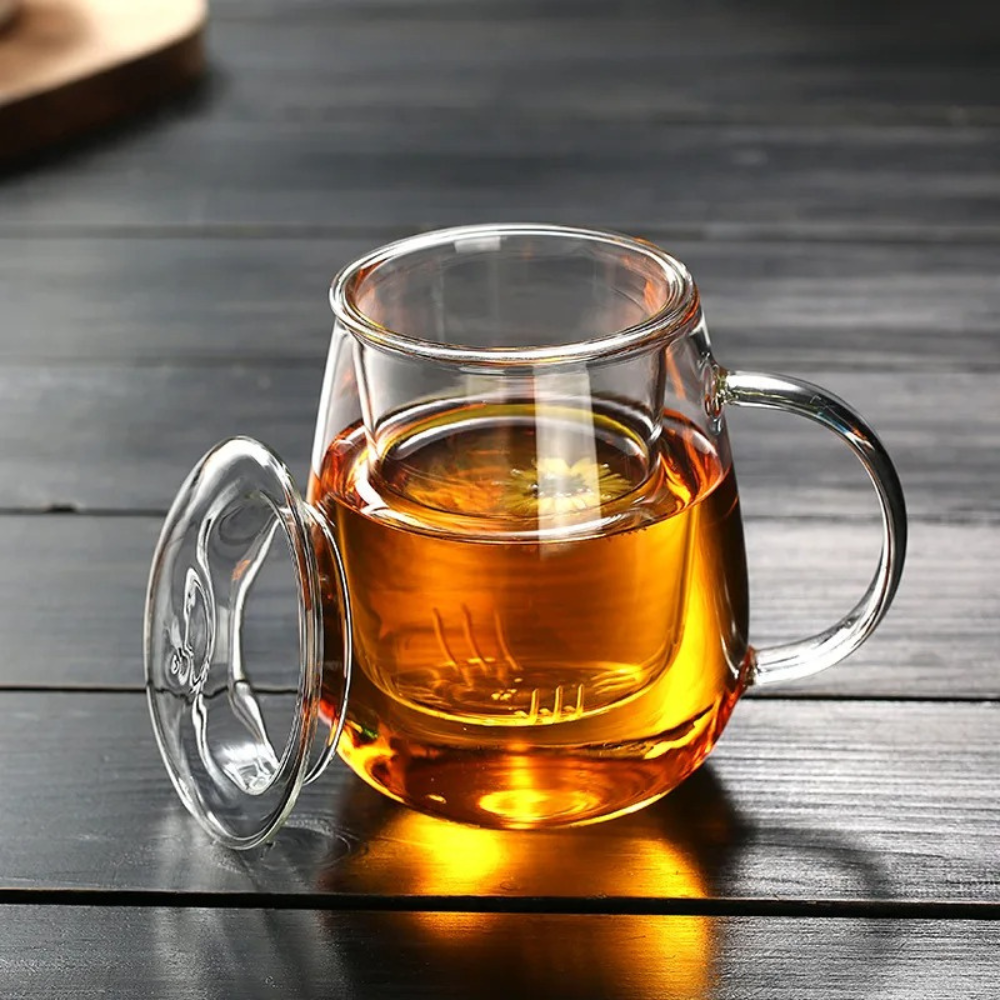 Small glass teapot with infuser and cup on white background