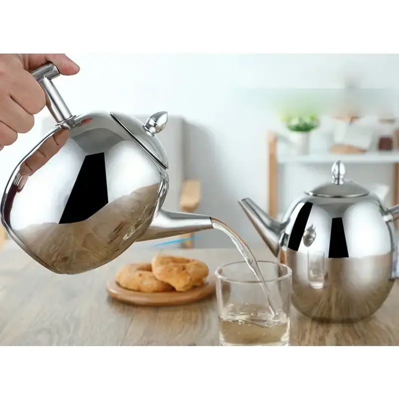 Stainless steel induction teapot with a brewed cup of tea beside it