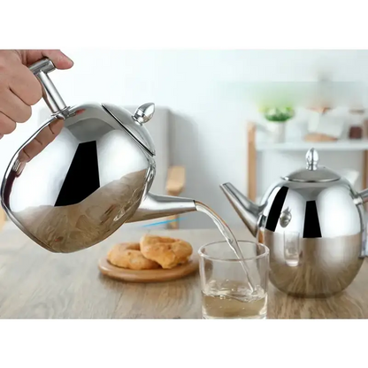 Stainless steel induction teapot with a brewed cup of tea beside it