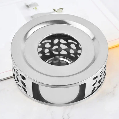 Silver finish stainless steel teapot warmer with candle glow, tea ritual table scene