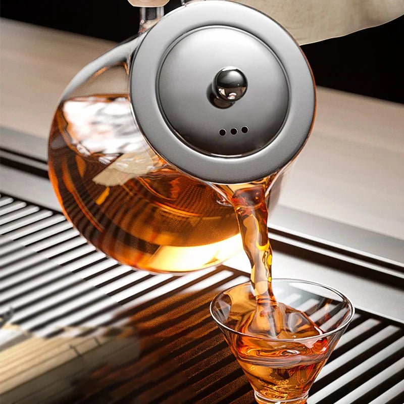 Stainless steel loose leaf teapot next to a freshly brewed cup of tea