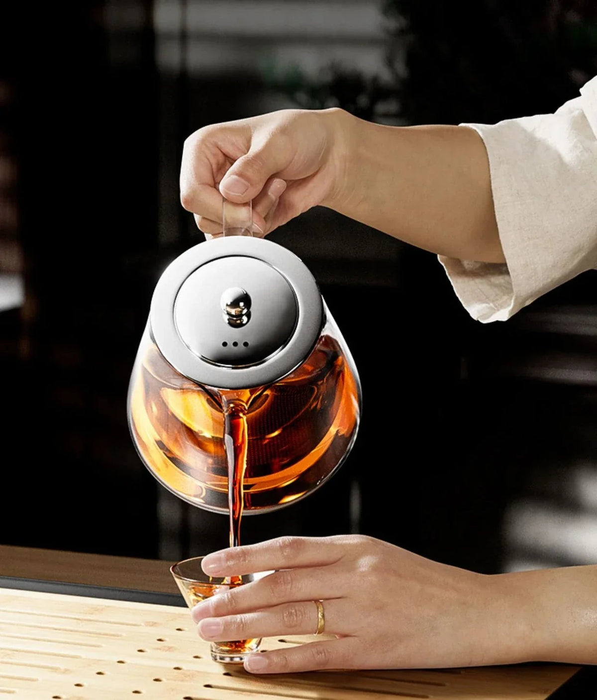Close-up of hot tea being poured from a stainless steel teapot into a ceramic mug