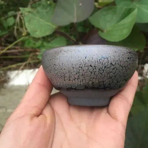 Earthy tenmoku ceramic tea cup with iron-spot glaze, side view