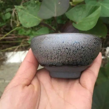Earthy tenmoku ceramic tea cup with iron-spot glaze, side view