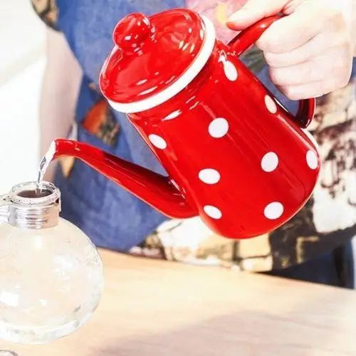 Pouring hot water from red polka dot stovetop kettle into teacup