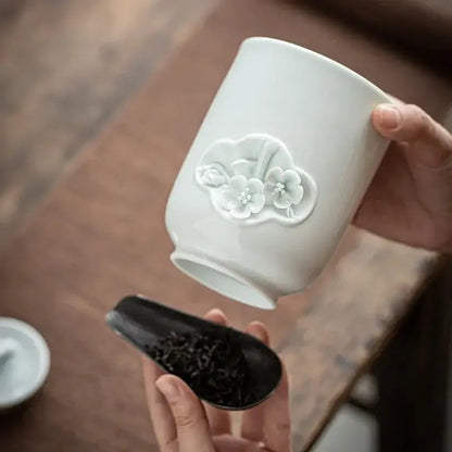 White ceramic tea storage canister on wooden shelf beside tea cups