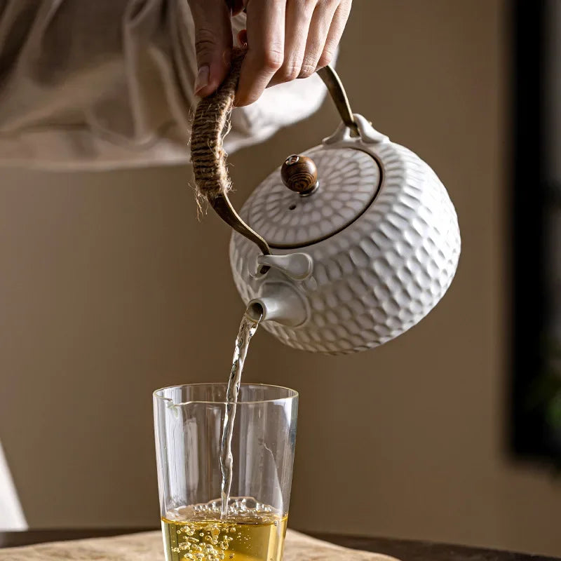 White ceramic teapot with braided rope handle on wooden table, side view