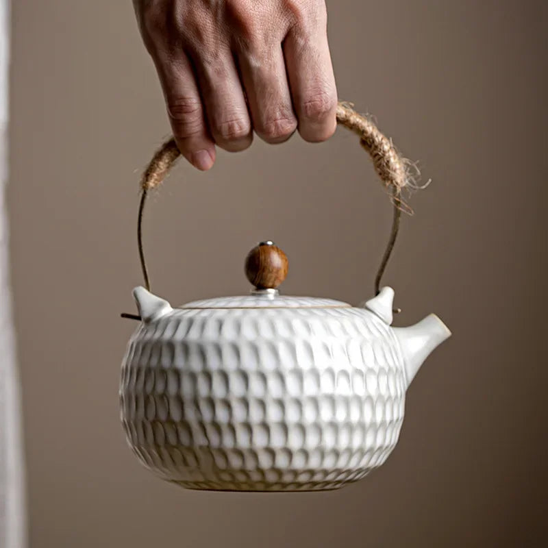 White ceramic teapot with rope handle pouring tea into a white cup