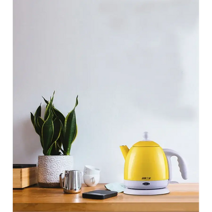 Yellow stainless steel electric kettle on wooden table beside a tea cup and saucer